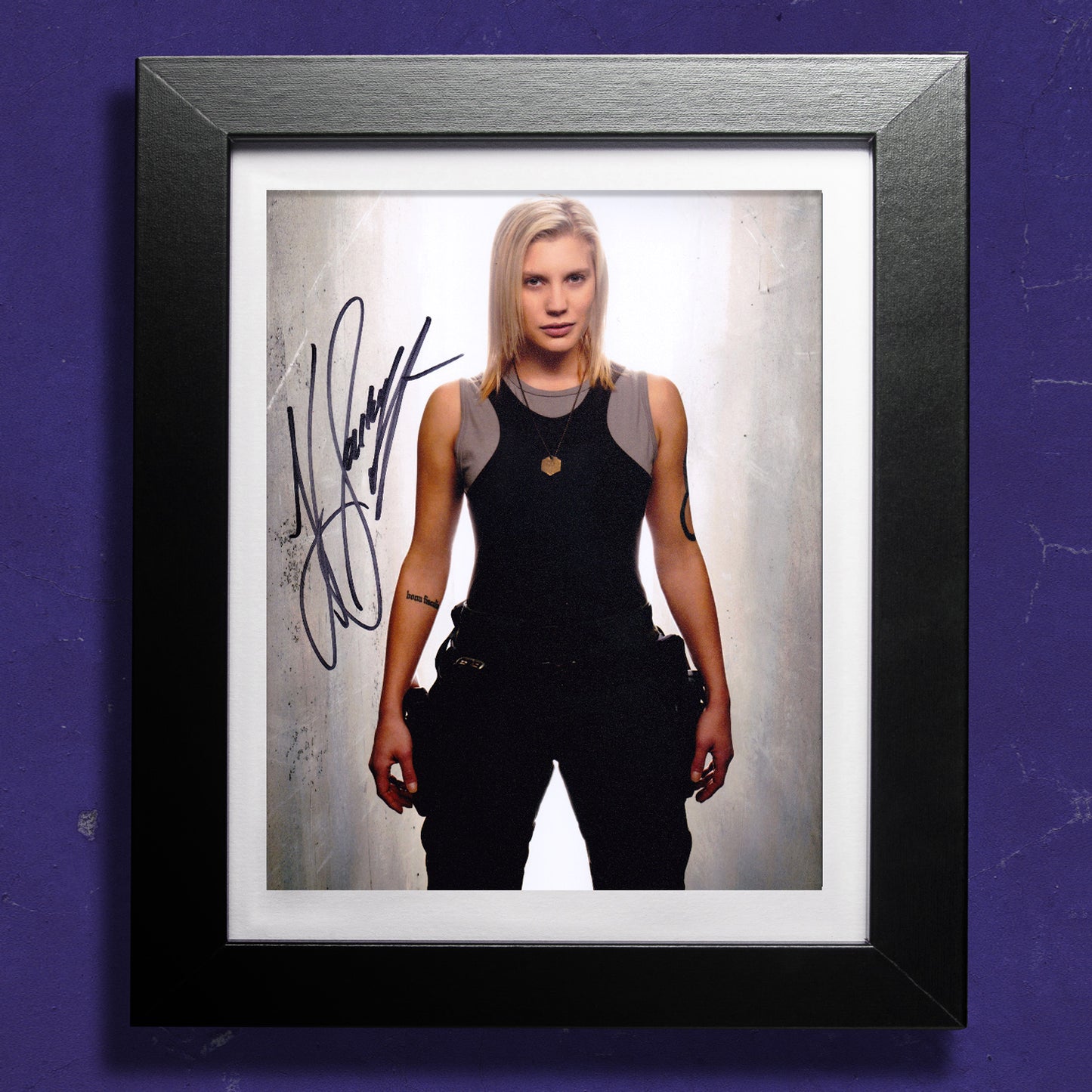 A framed image against a purple wall. The image shows actor Katee Sackhoff as the character Starbuck, from the TV series "Battlestar Galactica." Across the front of the image is Katee's autograph.