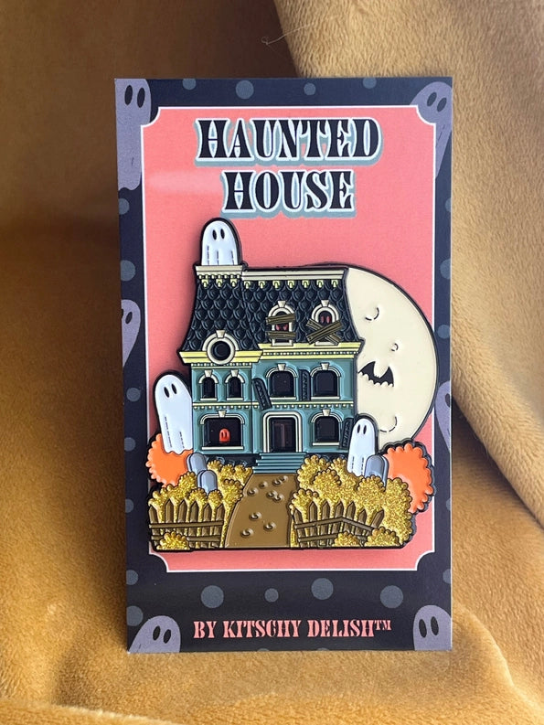 An enamel pin depicting a haunted house with a moon on the top corner