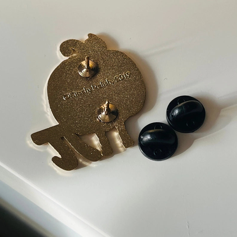 A gold glitter pinback charm shaped like a jack-o-lantern with a Pi symbol, shown on a white surface alongside two black round backing buttons.