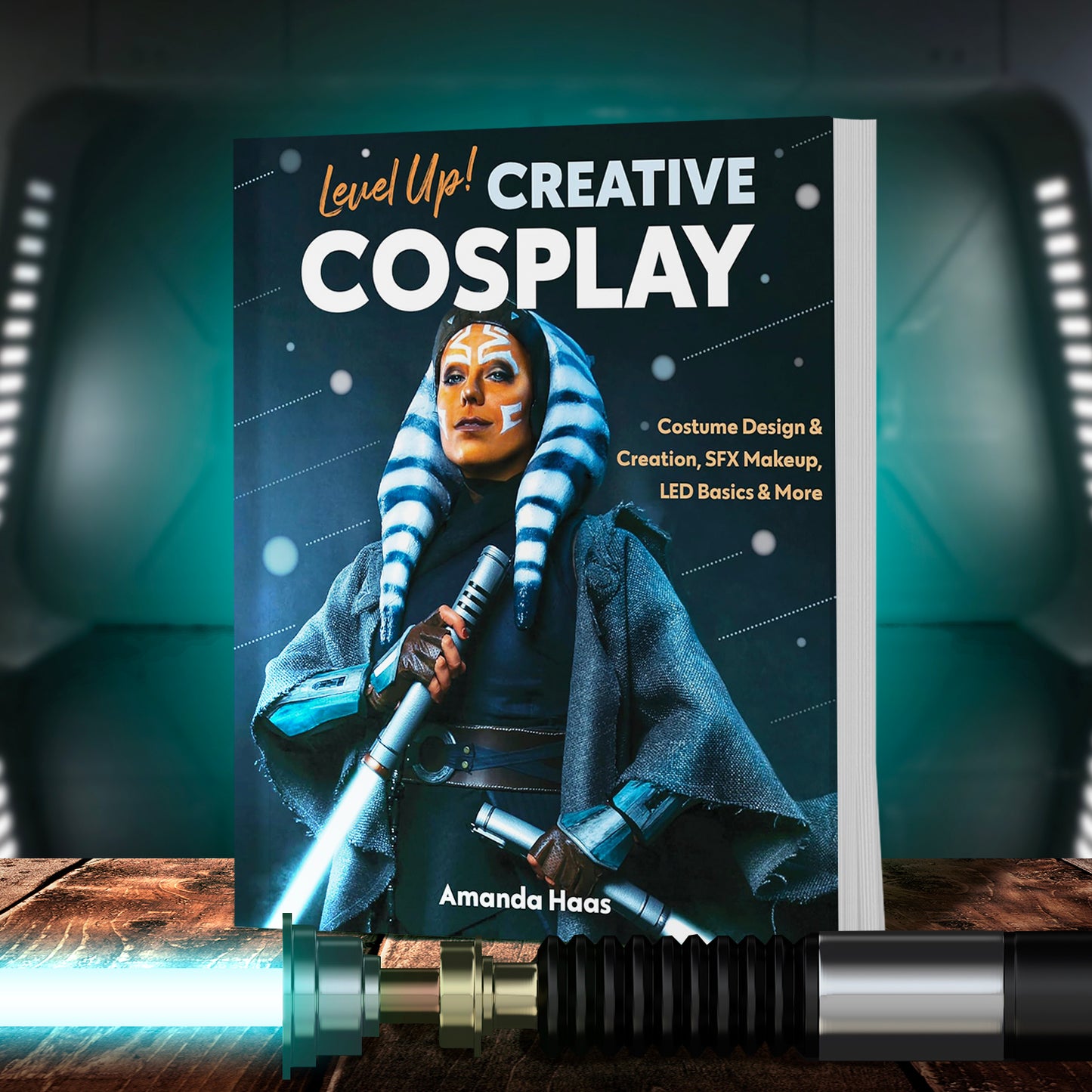 The cover image for "Level Up! Creative Cosplay" by Amanda Haas, depicting an Ahsoka cosplayer with two lightsabers. The book is standing on a wooden shelf. Below the book is an activated lightsaber. In the background is a sealed doorway in an Imperial base.