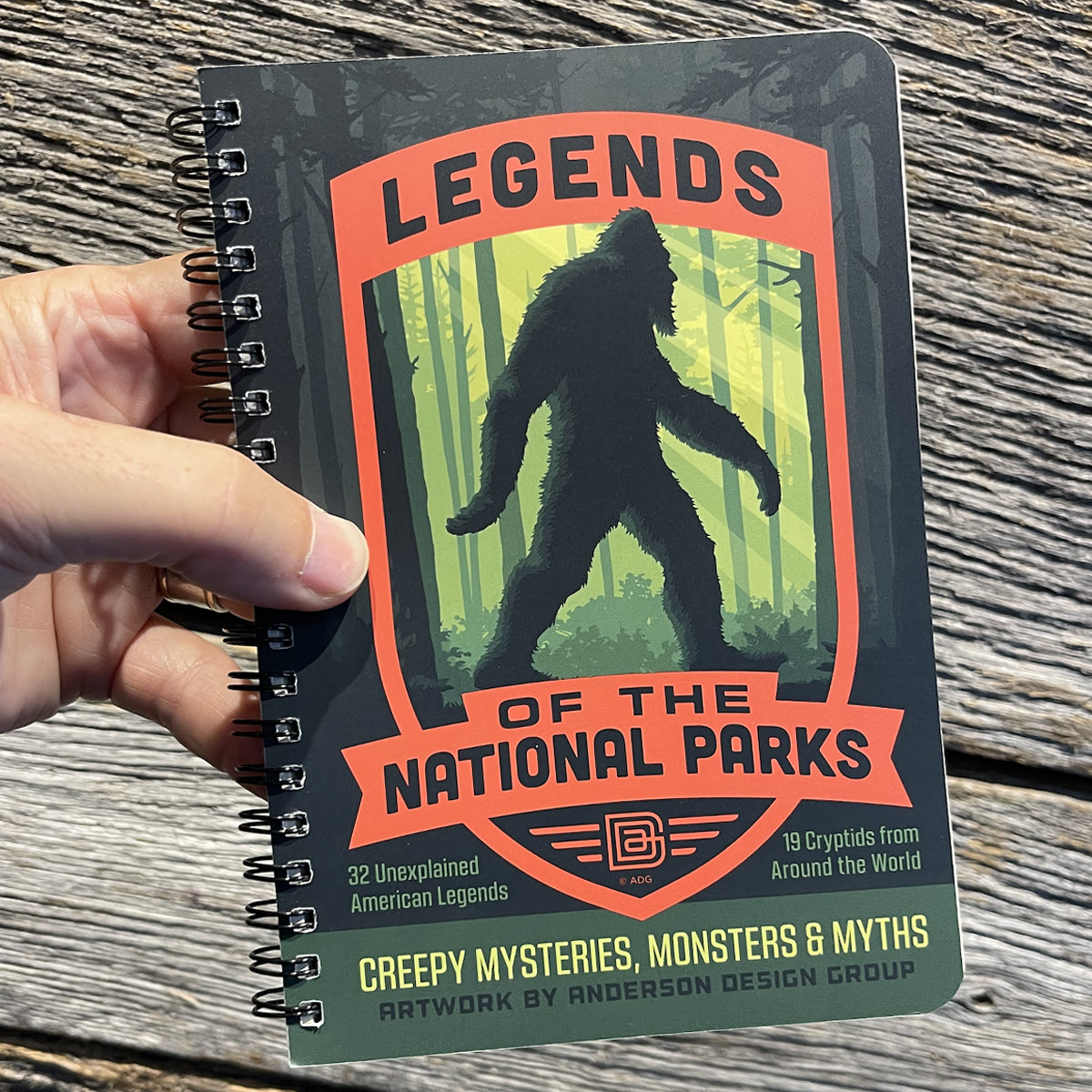 Notebook titled 'Legends of the National Parks' held by a hand on a wooden surface