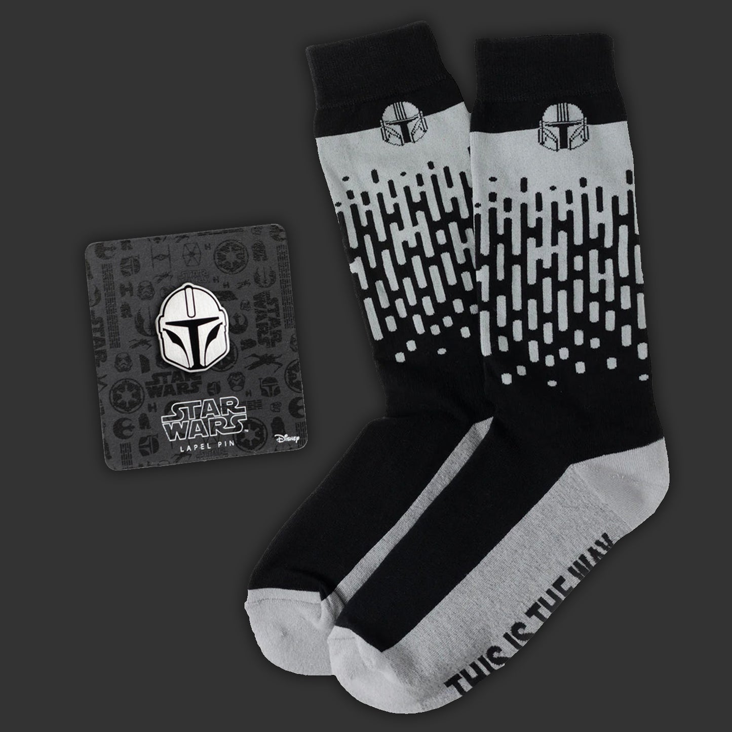 Black and gray socks with a pattern and 'This is the Way' text, alongside a matching Star Wars-themed lapel pin on a dark background.