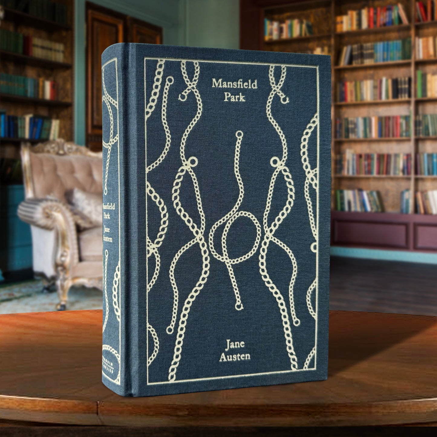 A clothbound hardcover copy of Jane Austen's MANSFIELD PARK, sitting in a rustic home library setting. The cover is a dark gray-blue with cream accents.