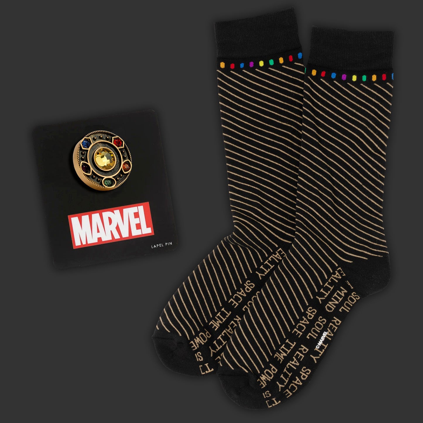 Marvel pin and black socks with gold text on a dark background. Next to the socks is a gold lapel pic depicting the Infinity stones