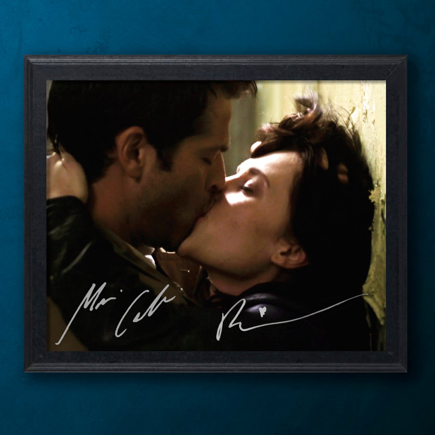 A framed still image from Supernatural showing Castiel and Meg kissing. Behind the image os a blue background.