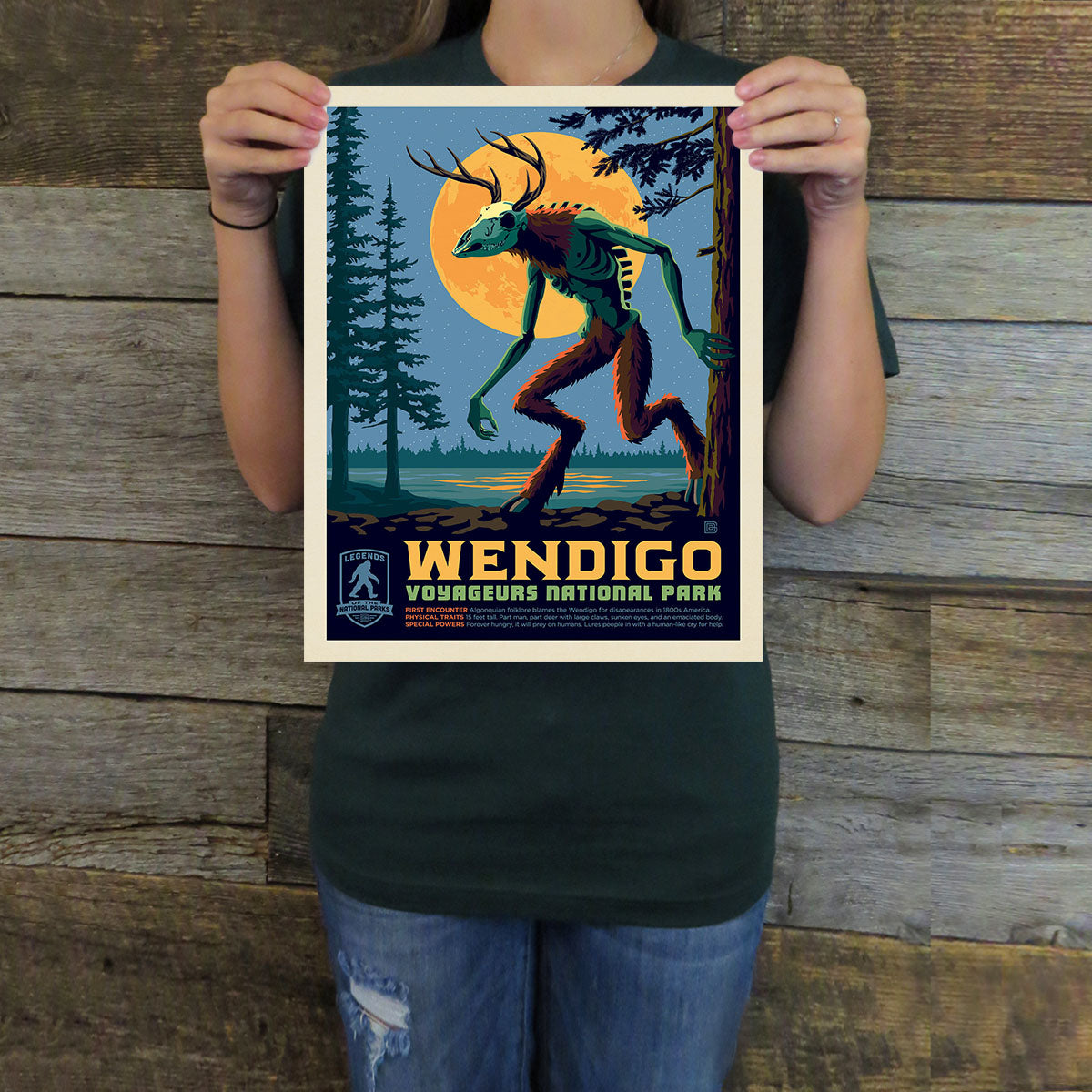 Person holding a poster of a Wendigo creature with a forest and moon background.