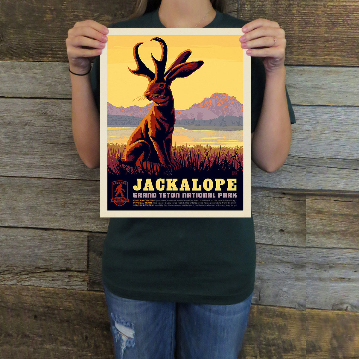 Person holding a Jackalope poster with a scenic background