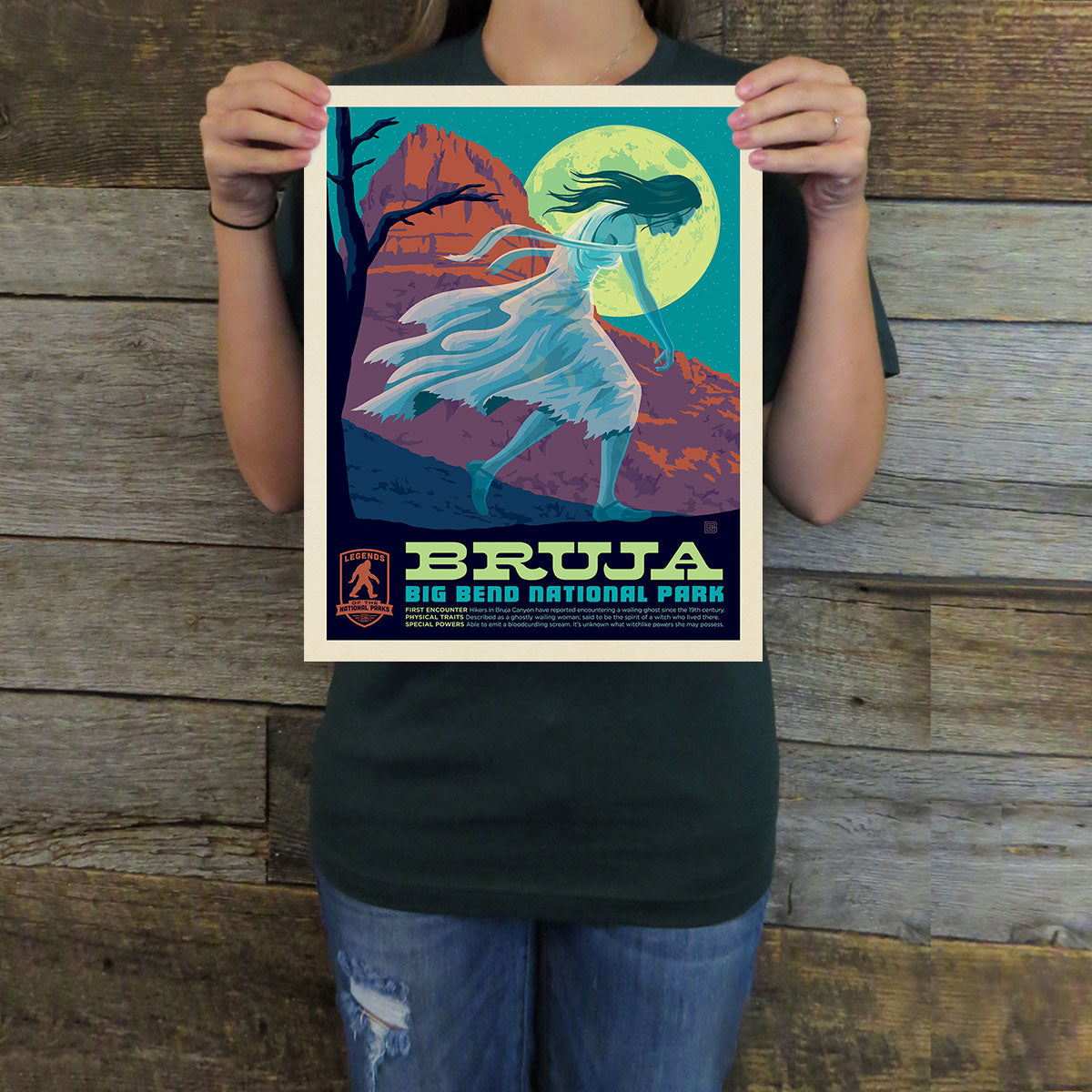 Person holding a 'Bruja Big Bend National Park' poster against a wooden background