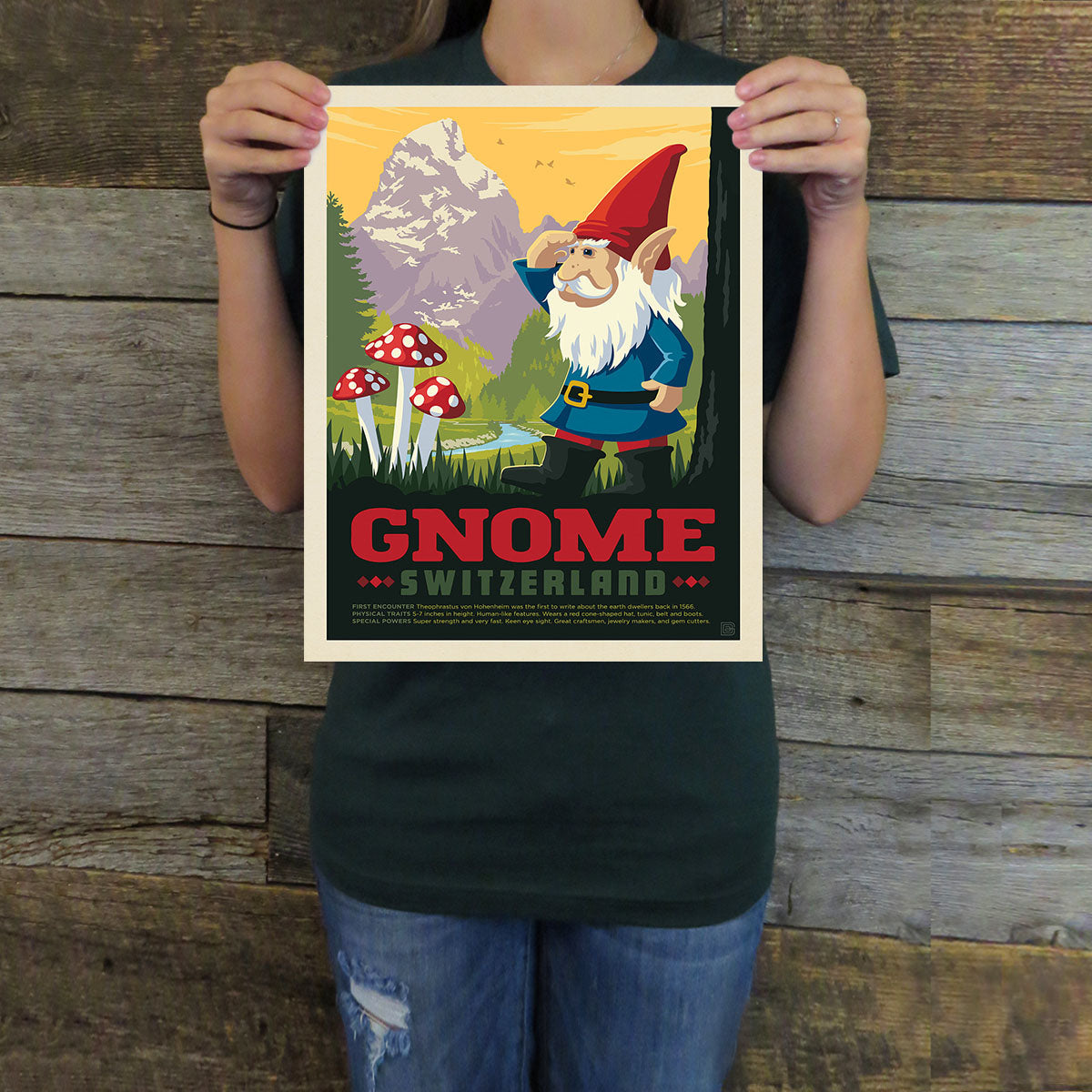 Person holding a poster of a gnome in a forest with mountains, mushrooms, and 'Gnome Switzerland' text.