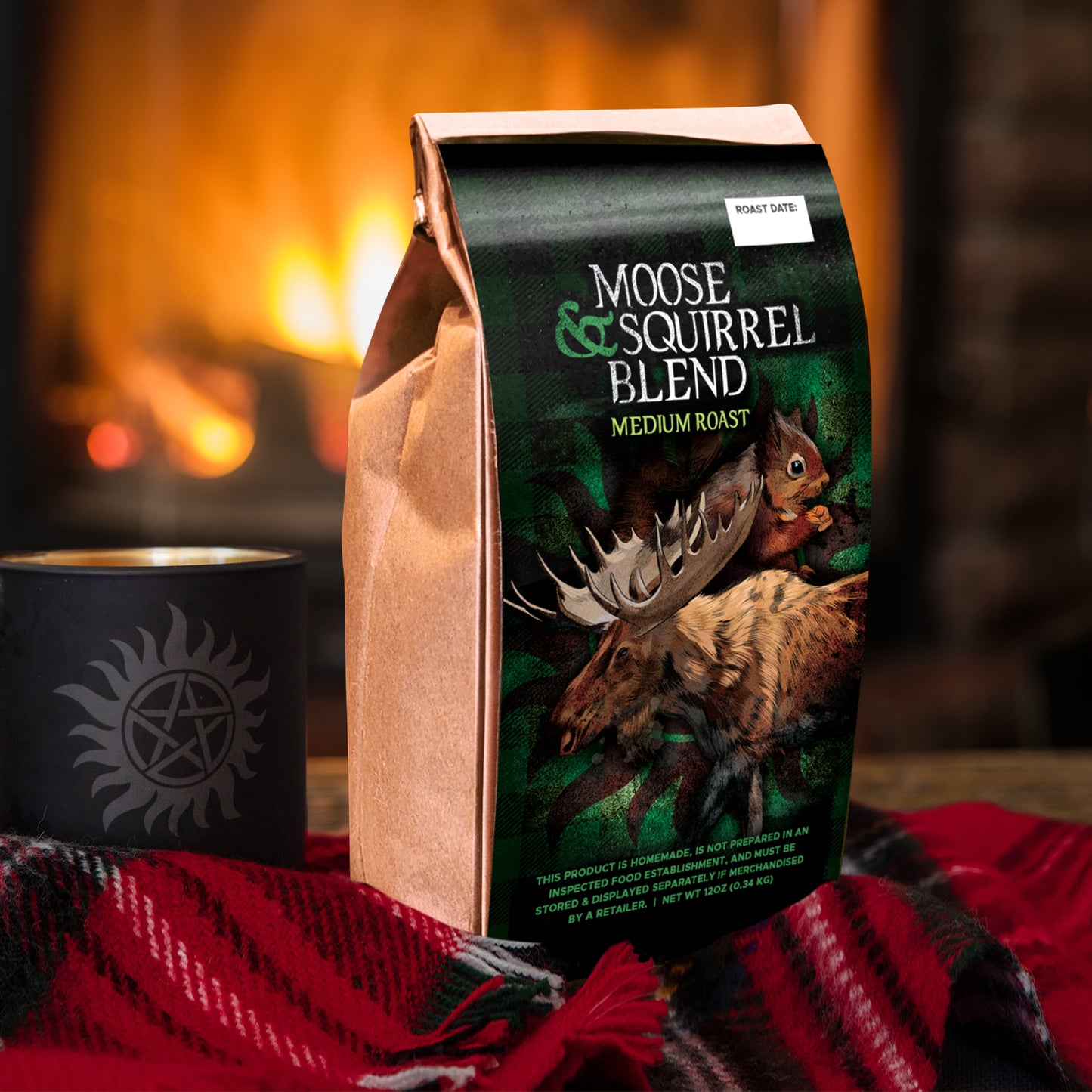 A paper coffee bag on a red, white, and black plaid blanket. The front of the bag depicts a moose and a squirrel in a green forest. Around them is a faint anti-possession symbol in black. White text at the top says "Moose & Squirrel blend medium roast." Next to the bag is a black coffee cup with a grey anti-possession symbol on the front. A fireplace is in the background.