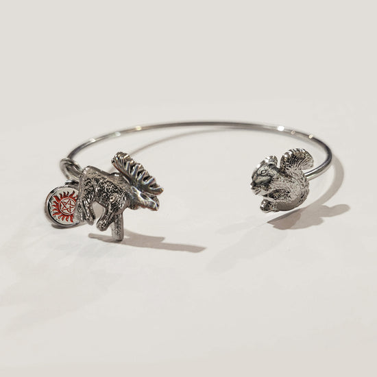 A silver bracelet against a white background. At each end of the bracelet are bangles. One is shaped like a squirrel, the other is a moose with an anti-possession charm attached to it.