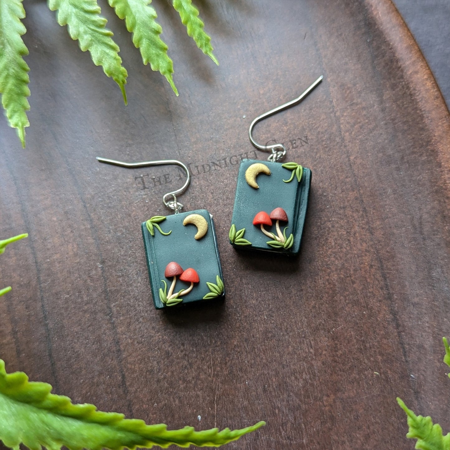 A pair of dangle earrings shaped like books, with tiny moons and mushrooms on the front.