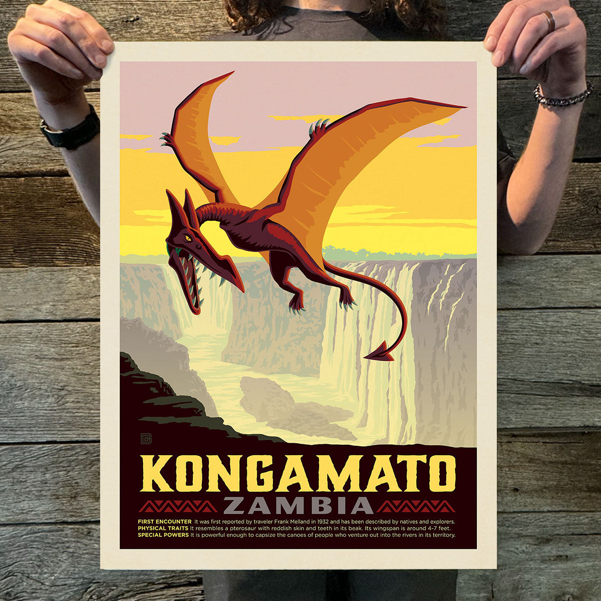 Person holding a poster of a dragon with 'Kongamato Zambia' text on a wooden surface