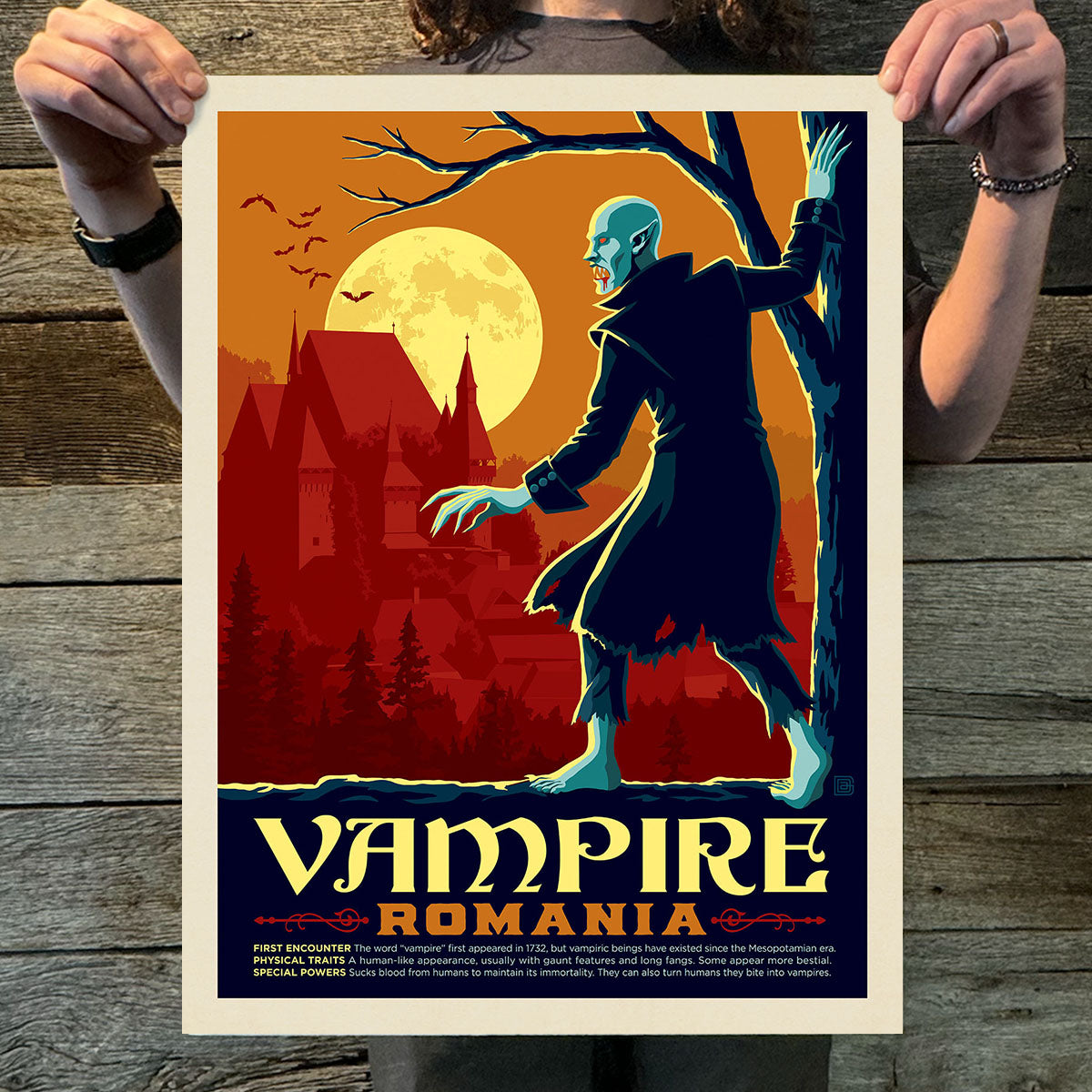 Poster of a vampire in a coat with a castle and moon in the background, held by two hands on a wooden surface.