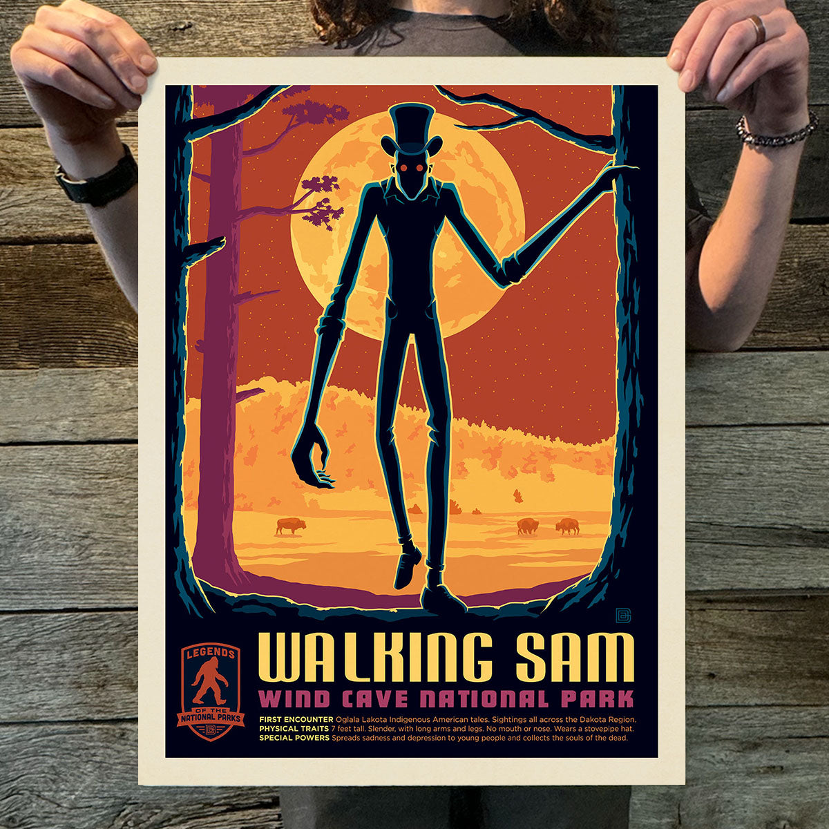 Person holding a 'Walking Sam' poster for Wind Cave National Park against a wooden background