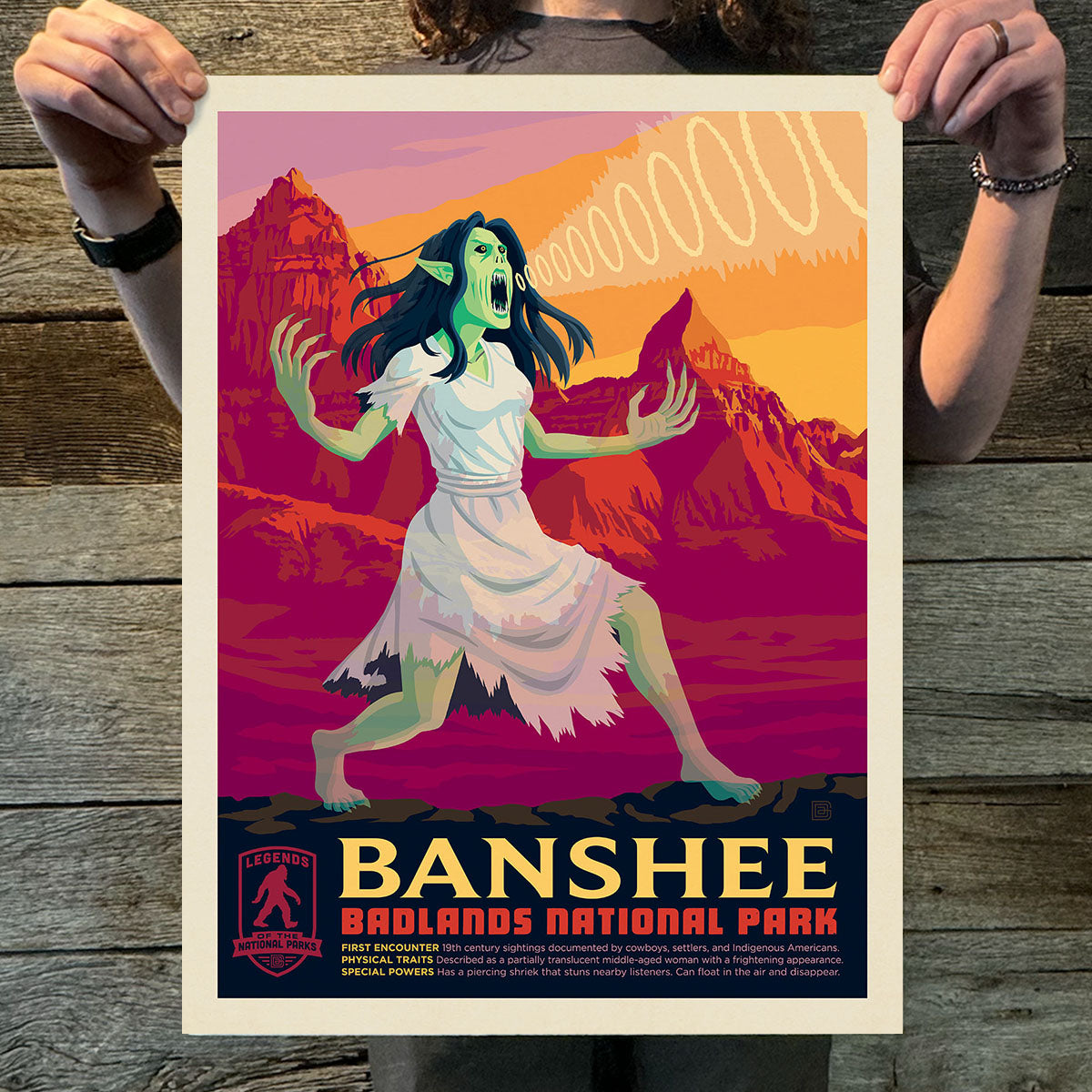 Poster of a banshee in a colorful design held by a person on a wooden surface