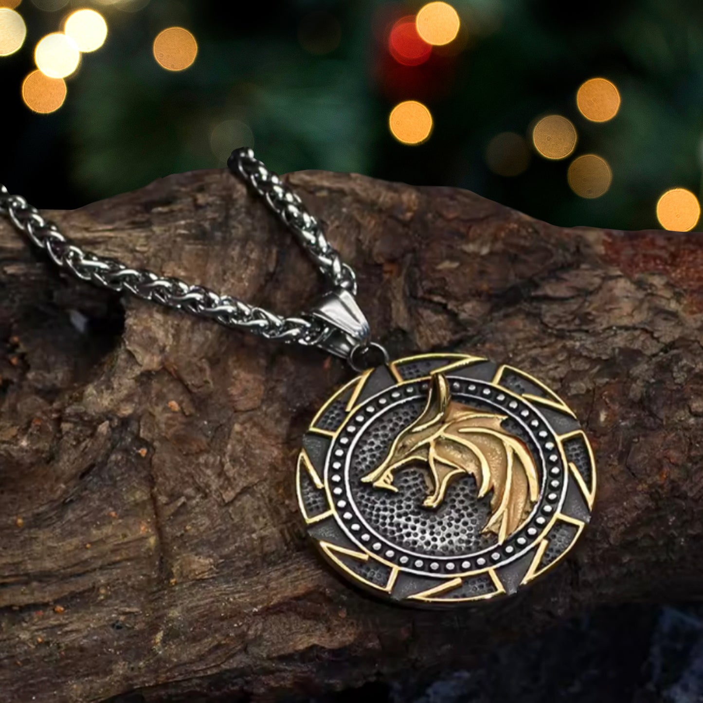 Close up of a black and gold pendant on a silver chain, resting on a tree limb. The pendant depicts a gold wolf head on a black round background. Around the edges is a Nordic knot pattern etched in gold. In the background are colored lights.