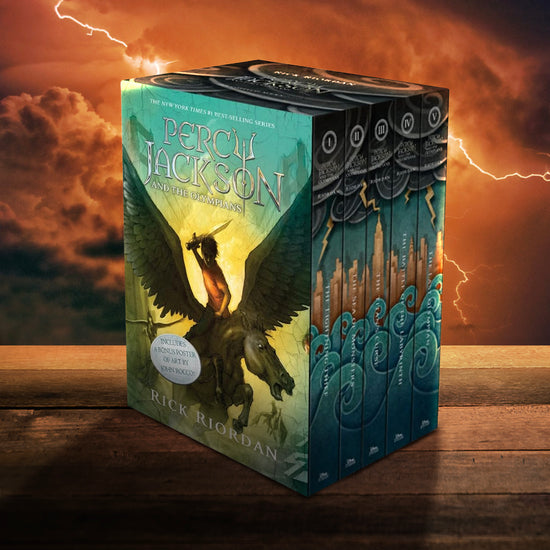 The boxed set of Percy Jackson and the Olympians featuring the original 5 books in the series with green-toned covers. The set is sitting on a wooden table, with a red-orange sky in the background. Bolts of lightning cross the sky.