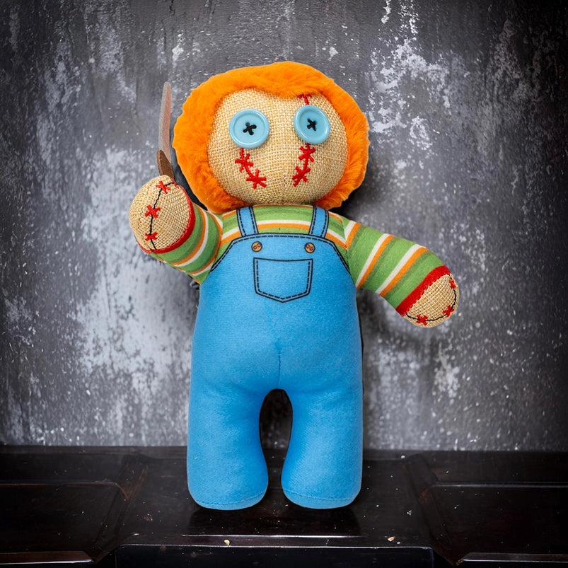 Toy figure with orange hair, blue eyes, and blue overalls holding a knife against a textured gray background.