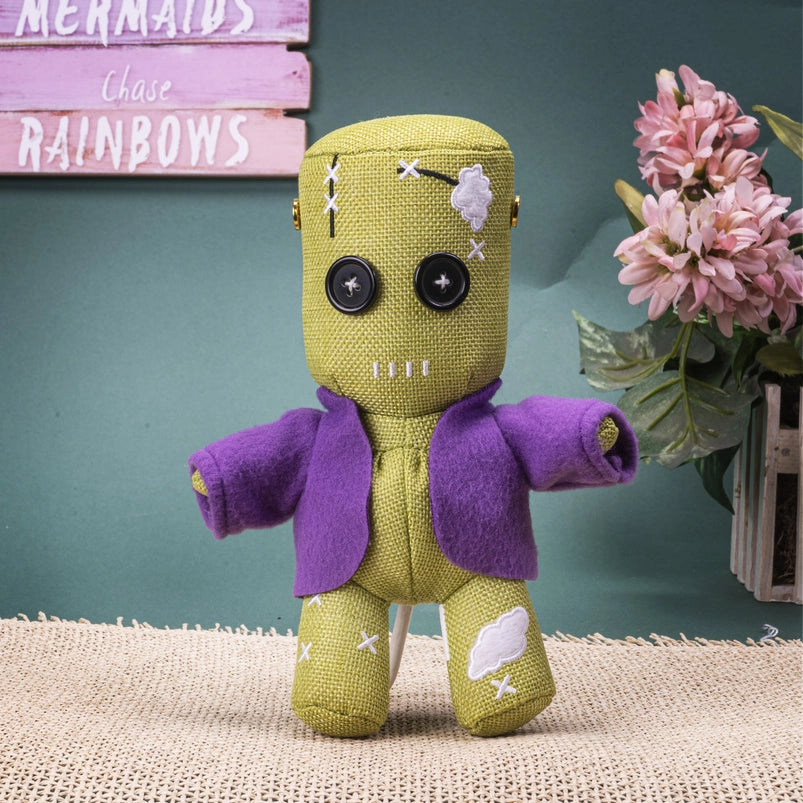 Green plush toy with a purple coat on a textured surface with flowers and a sign in the background.