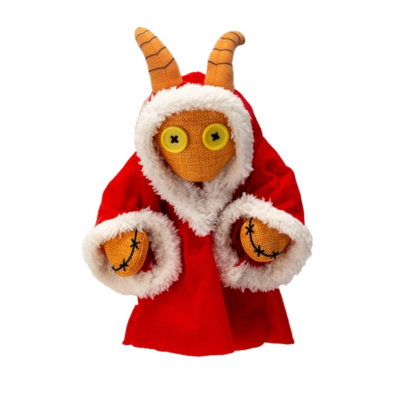 A stuffed plushie on a wooden table, against a white background. The plushie has yellow buttons as its eyes, and curled horns at the top of its head. It is wearing a red robe with white edges.