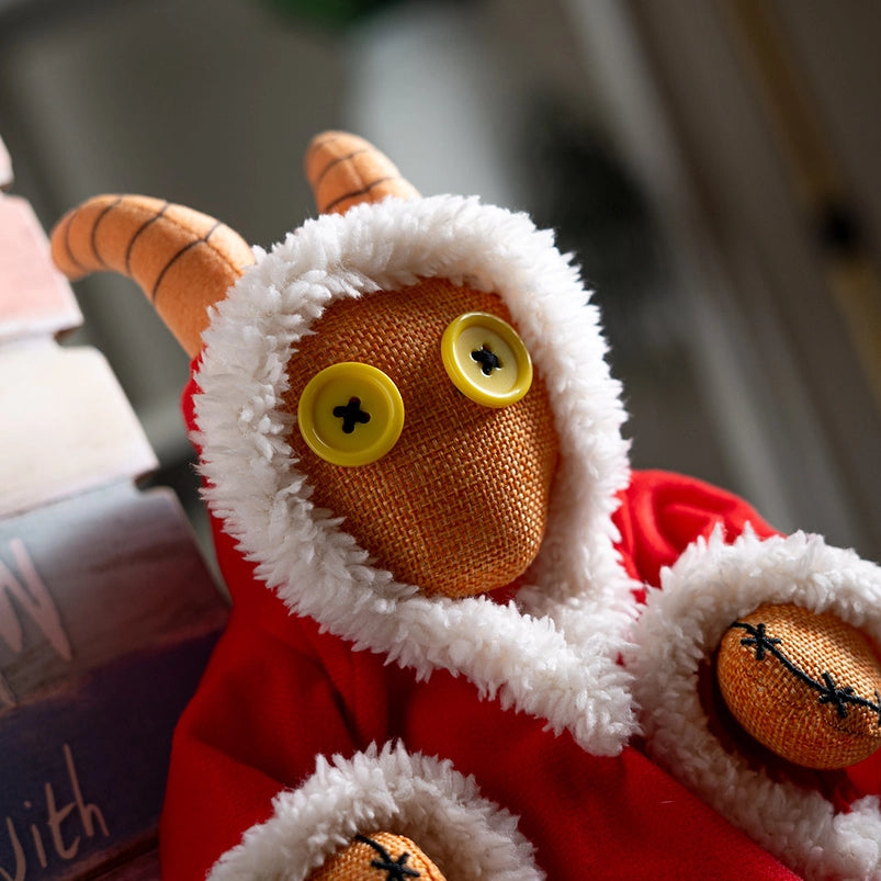 Close up of a stuffed plushie's face. The plushie has yellow buttons as its eyes, and is wearing a red robe with white edges.