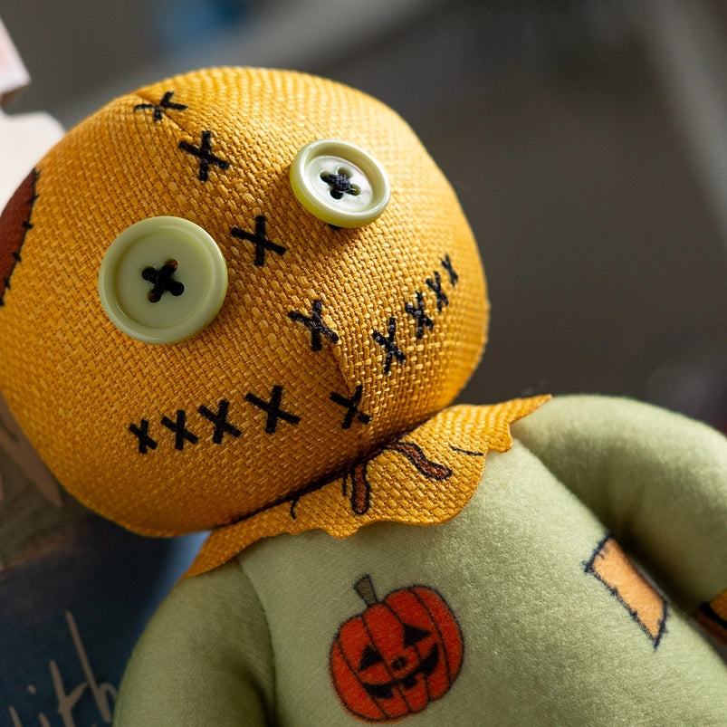 A stuffed plushie on a wooden table, against a white background. The plushie has light green buttons as its eyes, and is wearing a green jumpsuit with an orange sack as its head.
