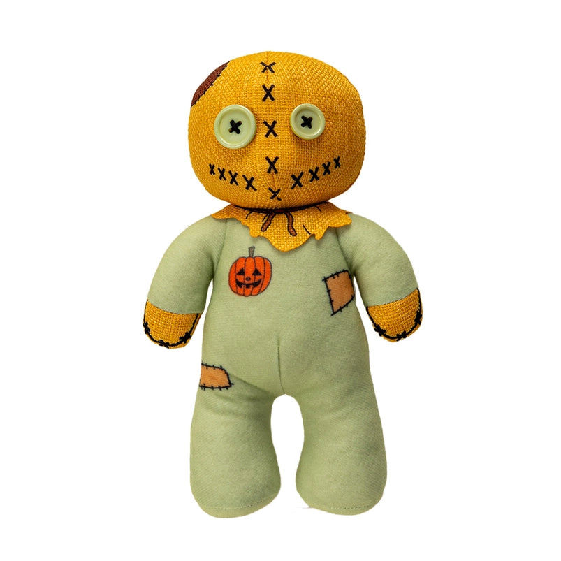 Close up of a plushie's face. The plushie has light green buttons as its eyes, and is wearing a green jumpsuit with an orange sack as its head.