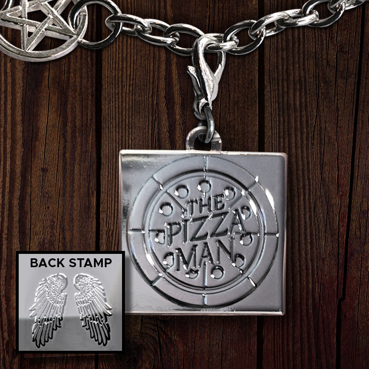 A metal charm against a wood background. The charm depicts a pizza box with "the pizza man" stamped on the front. On the back are a pair of angel wings