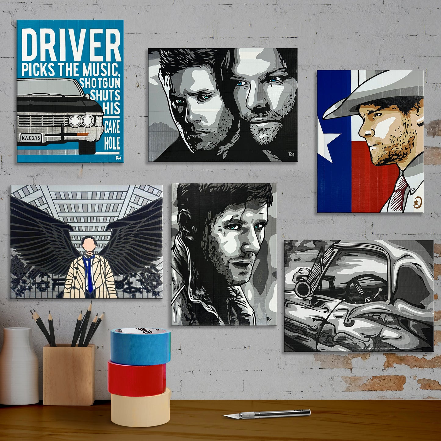 A white brick wall decorated with all 6 duct tape art pieces. From left to right, they are the "Driver picks the music" piece featuring the Impala, a greyscale close-up of the Winchester brothers, a side profile of Jared Padalecki as Walker in front of a Texan flag, a piece of Castiel standing with his wings spread in the barn, a shoulders-up greyscale piece of Dean Winchester, and a greyscale closeup of the side of the Impala.