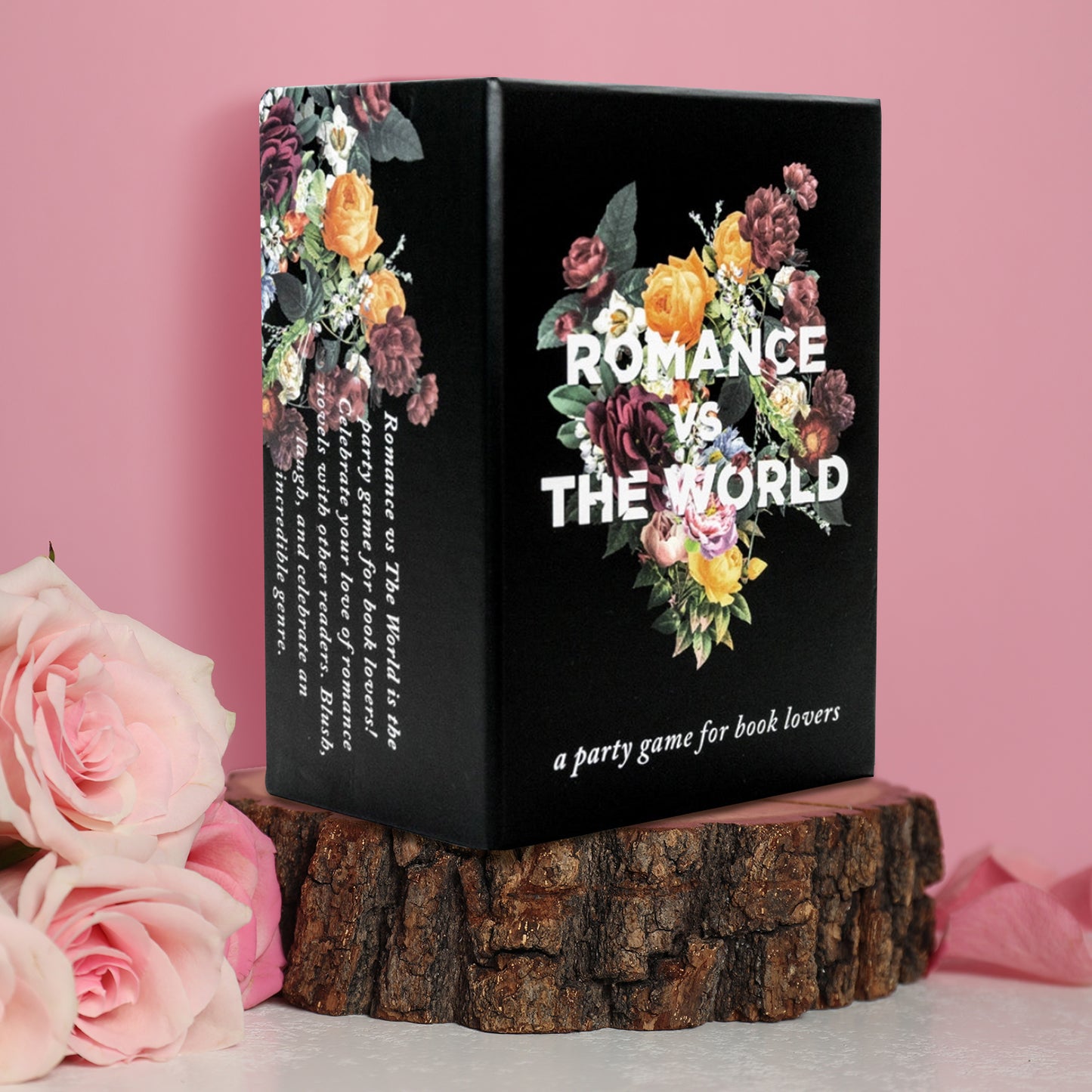 A black box on a piece of tree stump, sitting on a marble table. On the box cover is a bouquet of flowers, with white text in the center saying "romance vs the world." Behind the box is a pink background, with pink roses on the side.