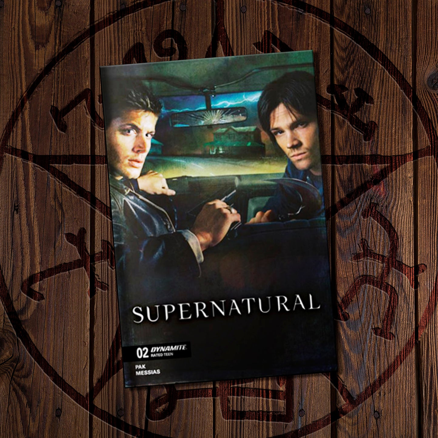 Supernatural comic book on a wooden background featuring a Devil's trap symbol. The cover depicts Sam and Dean in the front seat of a car.