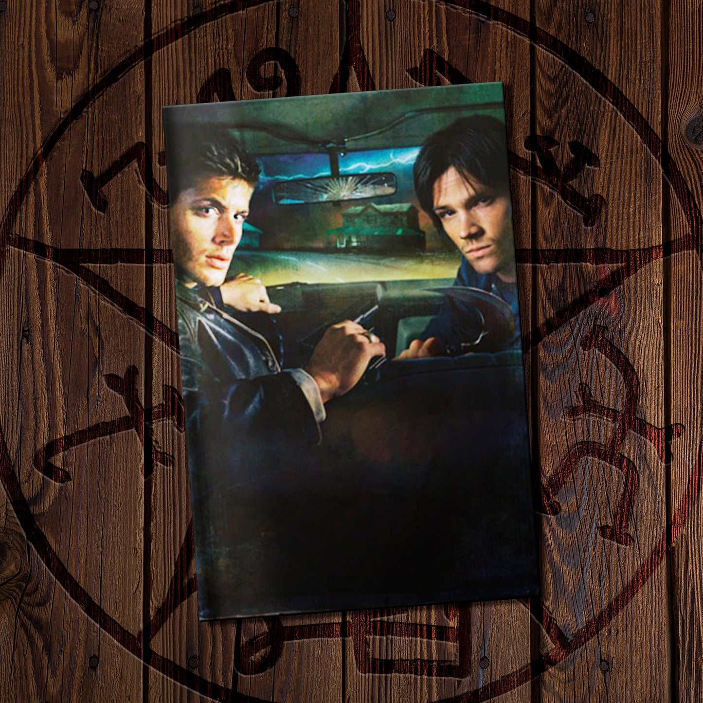 Supernatural comic book on a wooden background featuring a Devil's trap symbol. The cover depicts Sam and Dean in the front seat of a car.