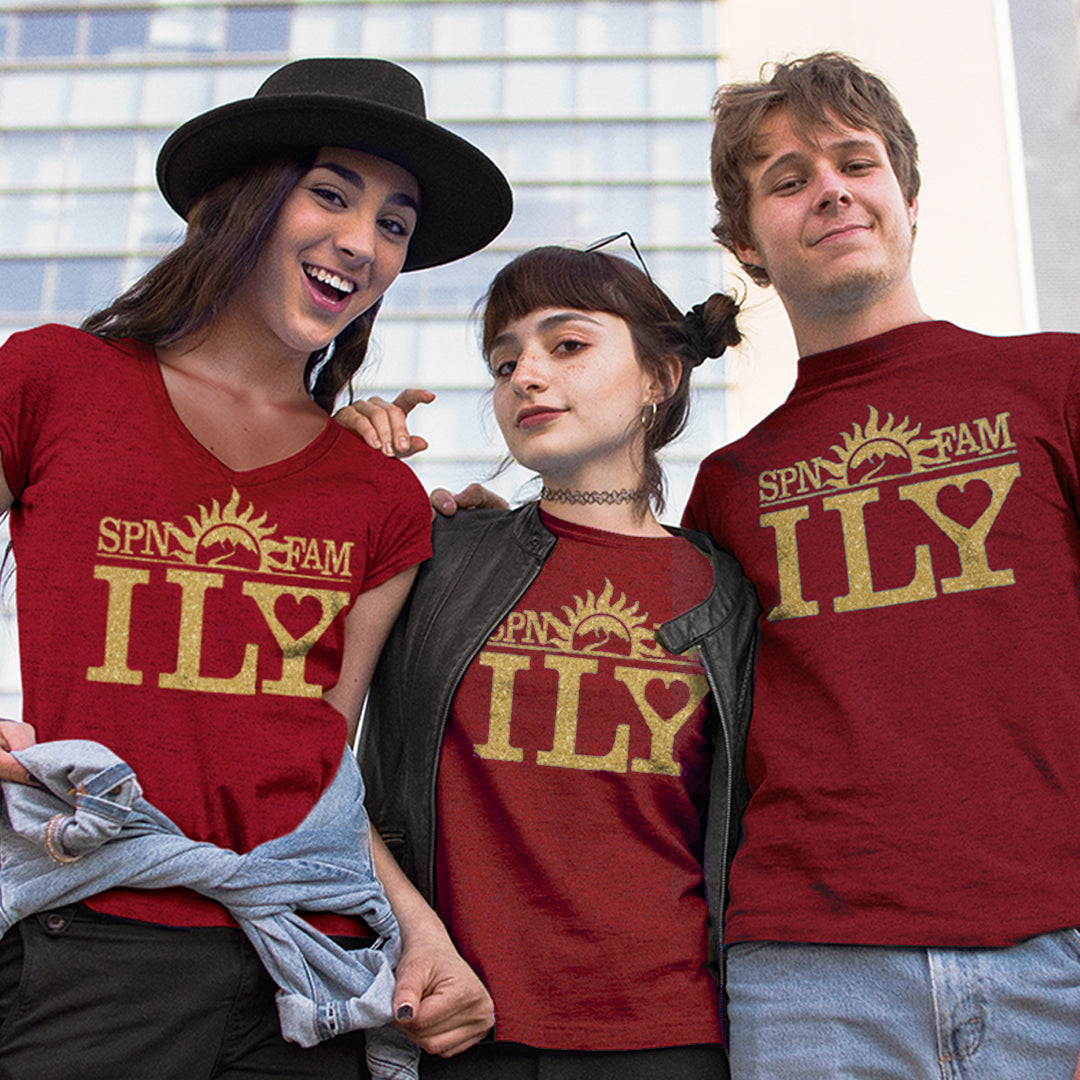 Two female models and one male model, all wearing dark red t-shirts. The shirts have gold text that says SPN FAM across the top, with ILY in larger font below. In the center is a rising sun image, with a road leading into the mountains.