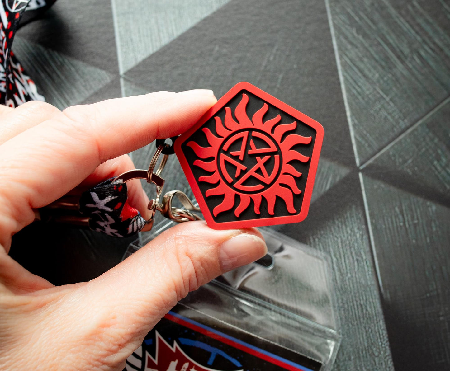 A model's hand holding an anti-possession charm in red and black. Under the charm is a black surface.