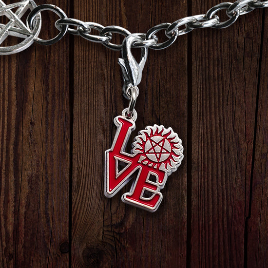 A red and silver charm against a wooden background, attached to a silver chain. The charm depicts the word Love" with the "O" replaced with the anti-possession symbol. 