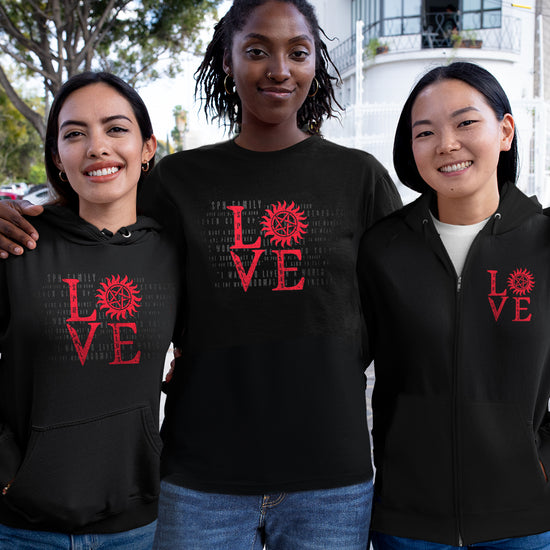 Three female models wearing black t-shirts and hoodies. Each garment has red lettering that says LOVE - the "o" is the anti-possession symbol. Behind the models is a street lined with trees.