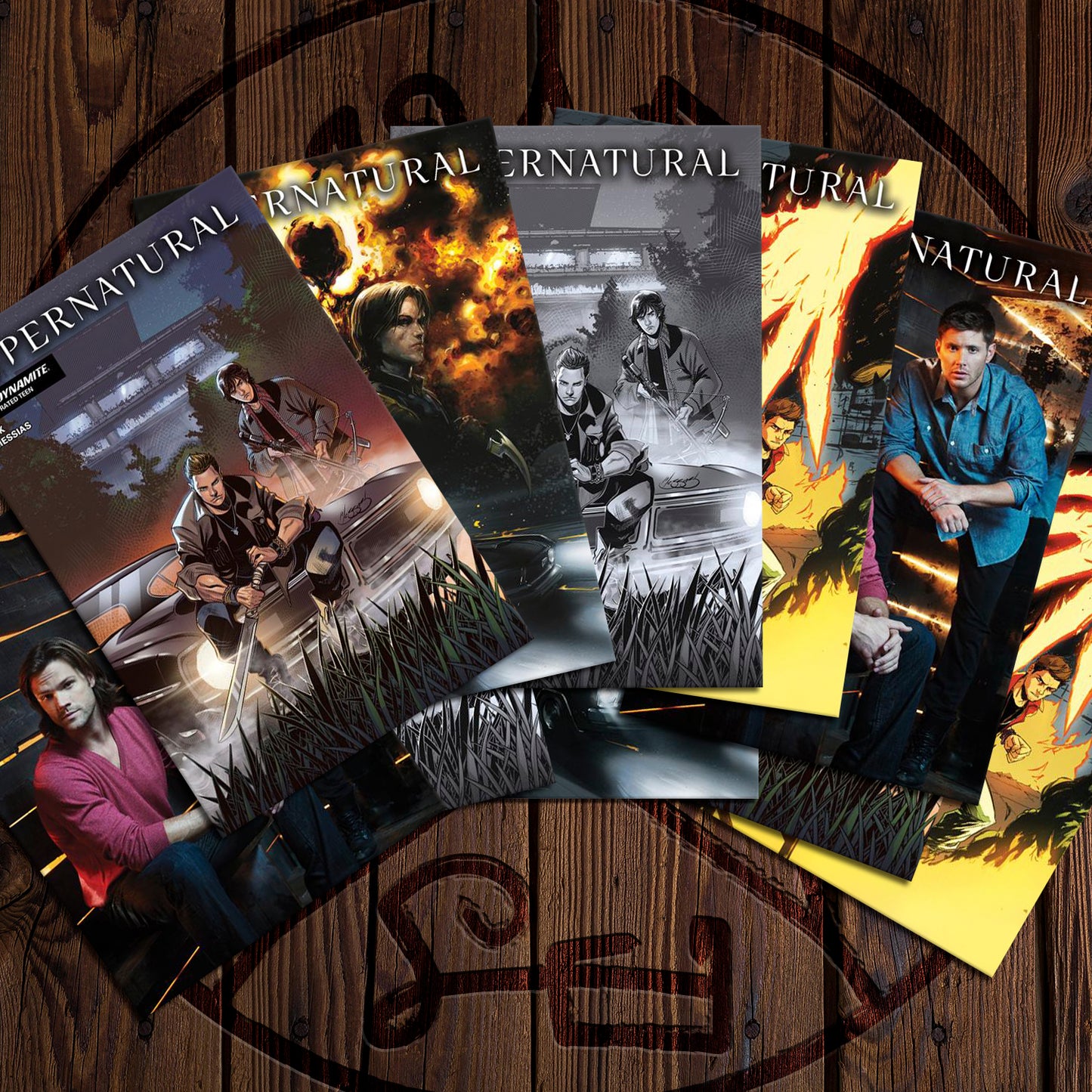 A collection of comic books on a wooden floor. Each comic depicts a different front cover of Supernatural Issue #1. Etched into the floor is a Devil's Trap symbol.