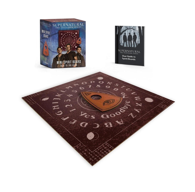 A brown ouija board on a white background. In the center is a wooden planchette. Behind the board is a book with instructions, and a cardboard box for the set. The box depicts Sam, Dean, and Castiel.