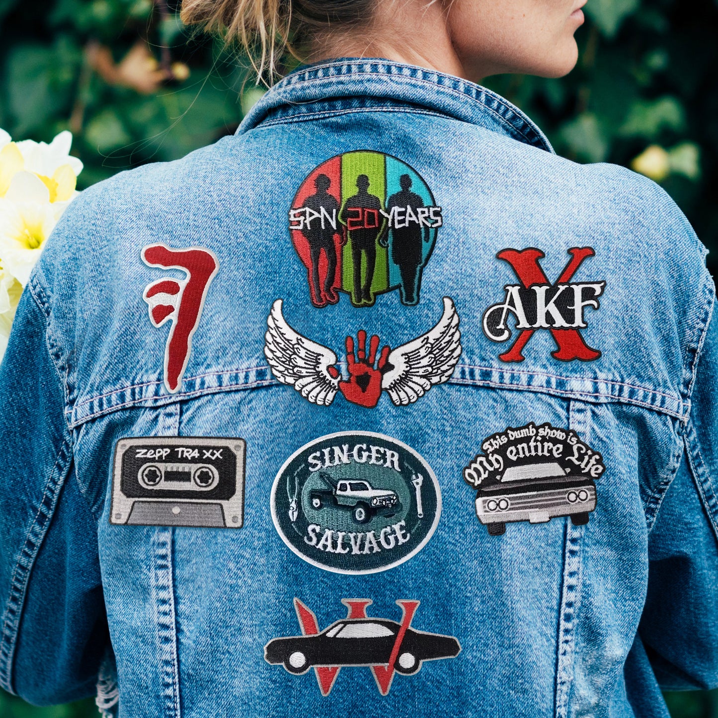 A model wearing a light blue denim jacket. Scattered across her back are various Supernatural-themed patches.