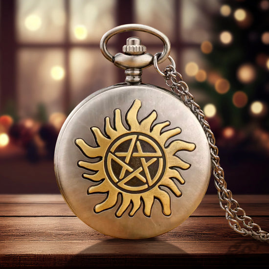 A silver pocket watch on a wood table. On the front of the pocket watch is the anti-possession symbol in gold. A silver chain is attached to the top of the watch. Behind the watch is a blurred Christmas tree next to windows.