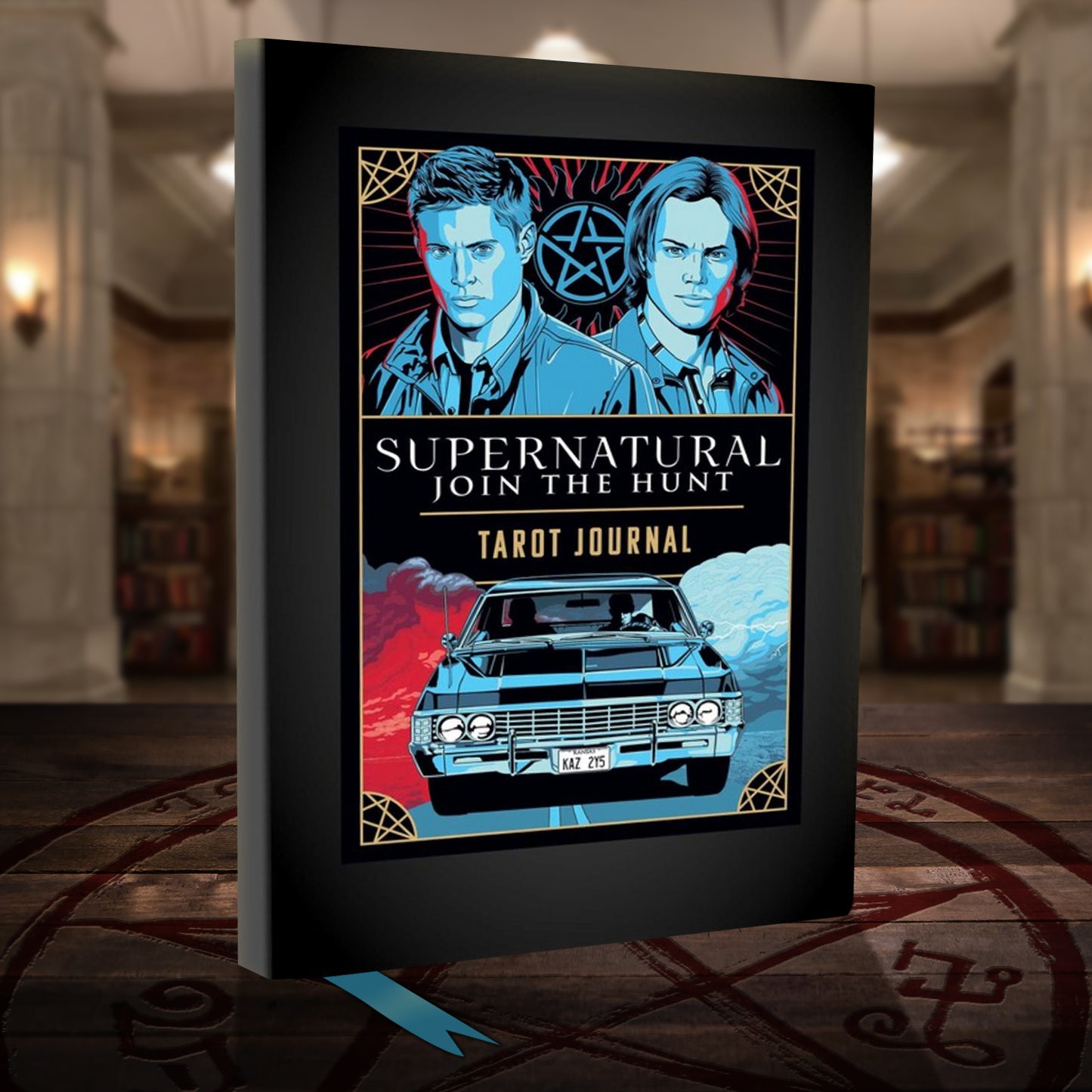 A black hardcover journal on a wooden table. The cover depicts blue and red drawings of Sam and Dean Winchester, with an anti-possession symbol between them. Underneath is a drawing of a black 1967 chevy impala. In the center is white and yellow text that says Supernatural, join the hunt. Tarot journal." Behind the book is The Bunker from the series