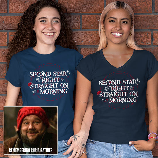 Two female models in front of a red brick wall. Their arms are linked, and they're each wearing a navy blue t-shirt. The shirt reads "Second star to the right and straight on 'til morning" in a white all-caps storybook font, with a thin red ring around it. The ring has small stars at two points and the "S" in "straight" has a red beanie cap hanging onto the top.