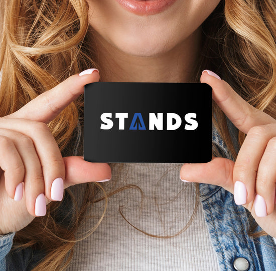 Close up of a female model holding a black gift card. On the front of the card is the Stands logo in white and blue.