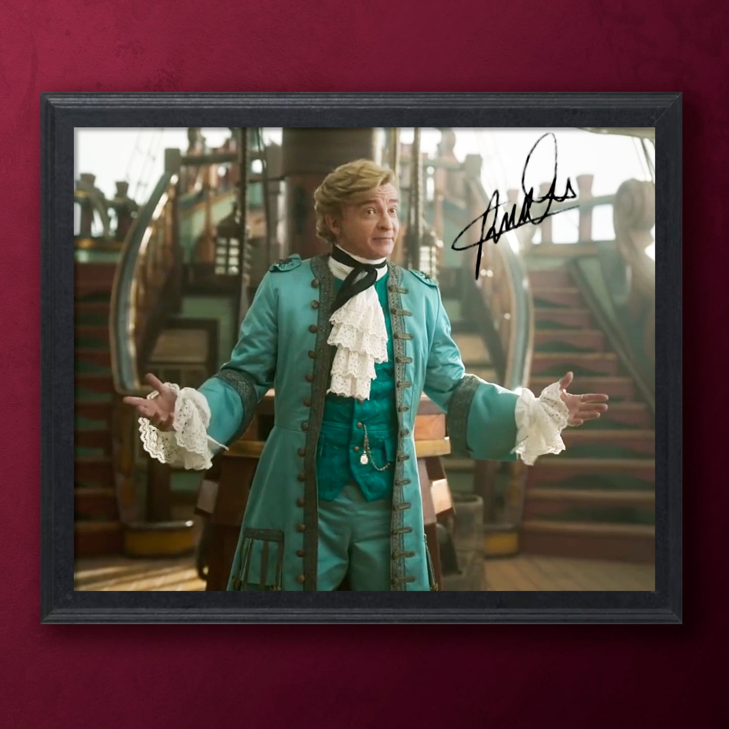 Framed photo of Rhys Darby in a teal costume with a signature on a red background