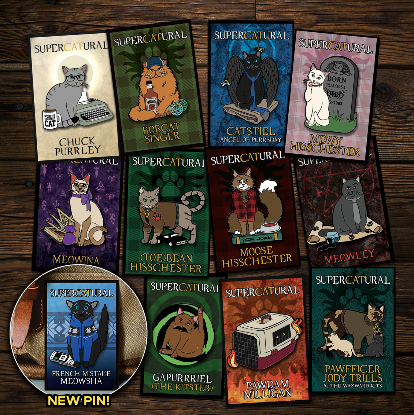 A collection of enamel pins on a wooden table. Each pin depicts a character from the TV series "Supernatural" reimagined as cats. An inset in the bottom left corner reads "NEW PIN!" and has an image of French Mistake Meowsha, the newest pin.