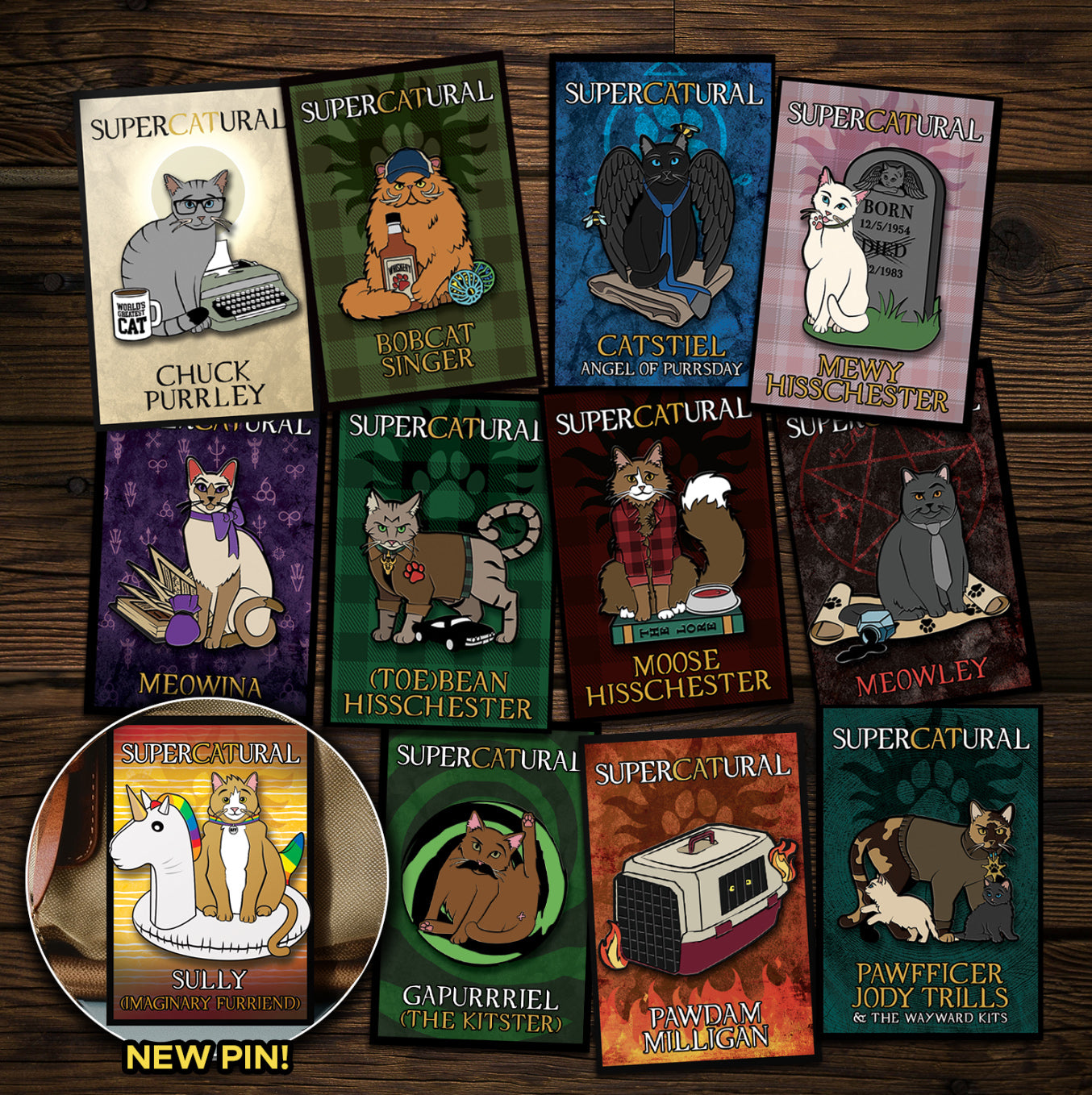 A collection of enamel pins on a wooden table. Each pin depicts a character from the TV series "Supernatural" reimagined as cats. An inset in the bottom left corner reads "NEW PIN!" and has an image of Sully, the newest pin.