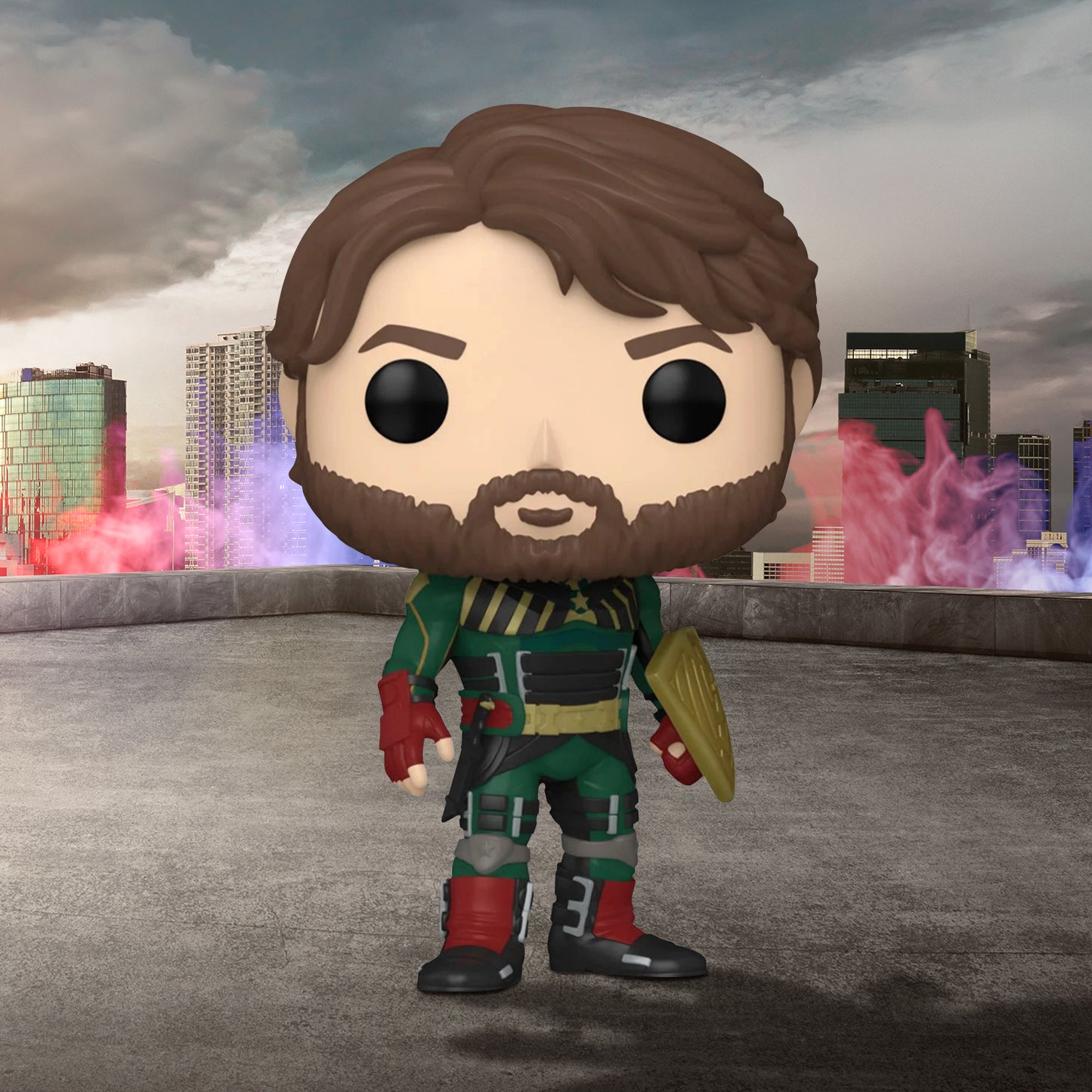 A vinyl Funko Pop figure of the character Soldier Boy from the TV series "The Boys," standing on a concrete rooftop. The figure has a brown beard, and is dressed in a green costume with a wedge-shaped shield on one forearm. In the background is a city skyline, with brightly covered smoke near the buildings.