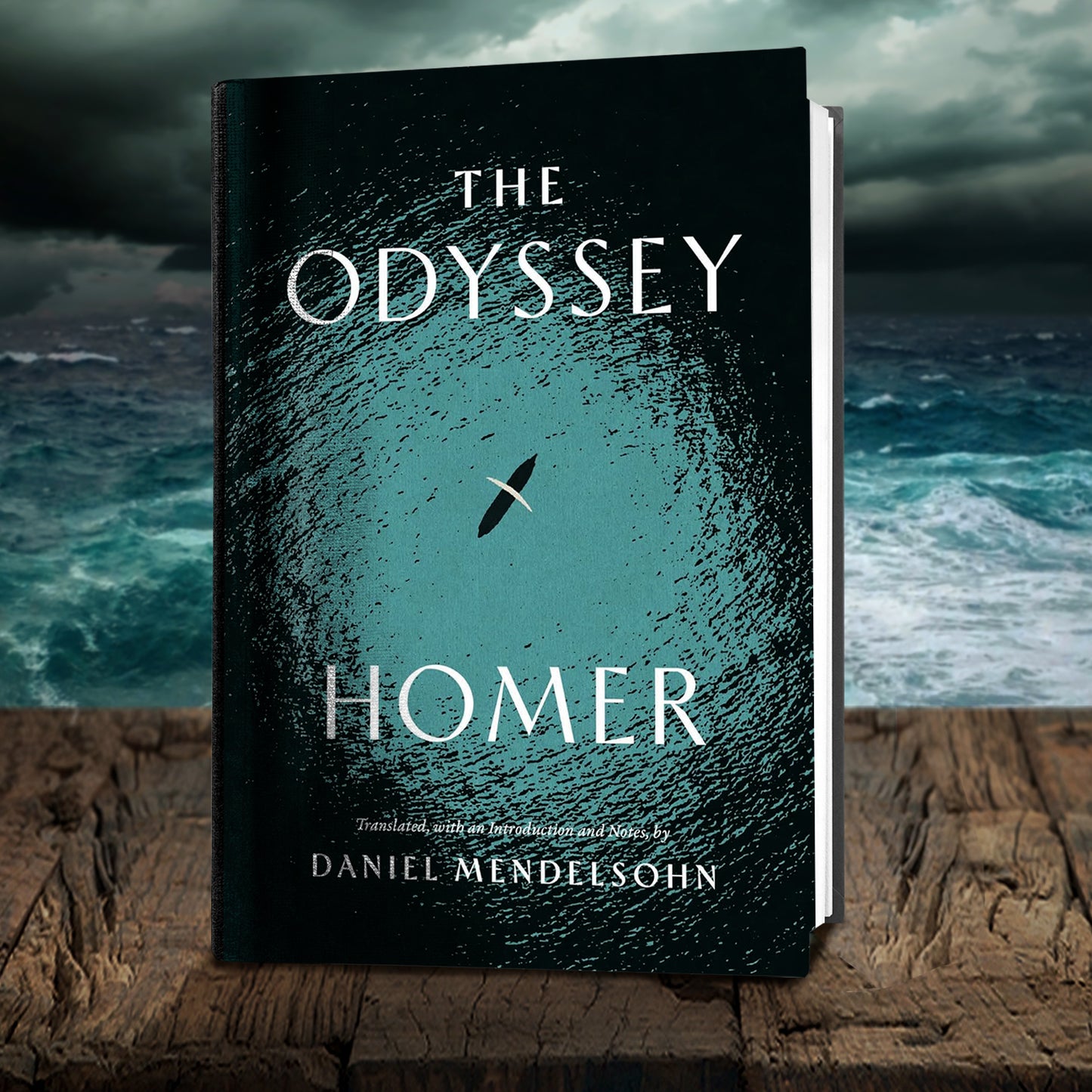 A hardcover book on a wooden ledge. On the front is a black and while silhouette image of an ancient boat and sail, on the ocean. White text says "The odyssey, Homer." Behind the book is the open ocean during a storm.