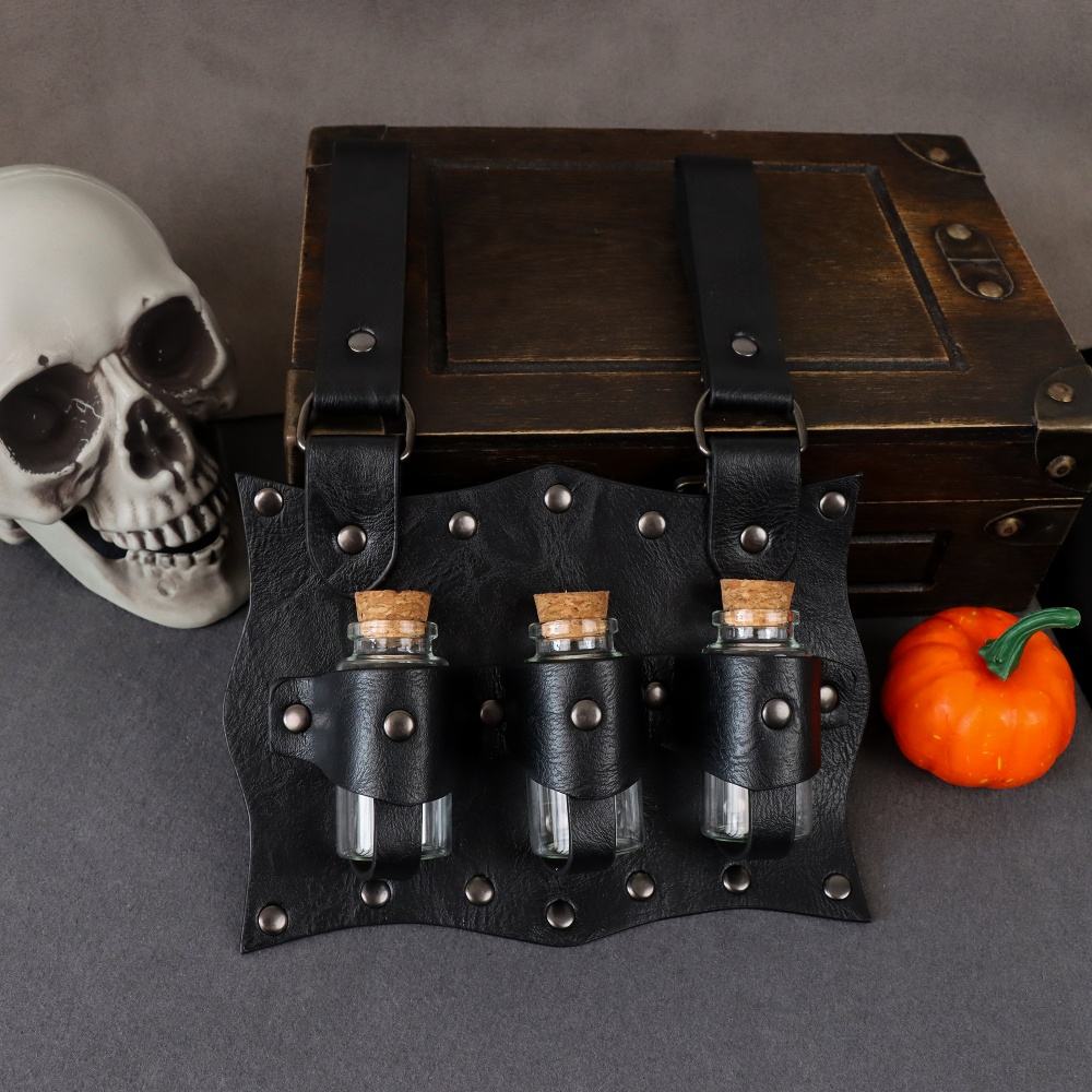 A black, leathery belt pack, with three glass bottles held in place with straps. The pack has two belt loops at the top. Behind the pack is a black box, with a skull and pumpkin on either side of it.